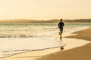 Junge läuft am Strand bei Sonnenuntergang - JOHF03979