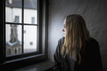 Young woman looking through window - JOHF04321