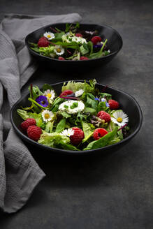 Schüssel mit frischem Salat mit Rucola, Spinat, Mangold, Eichblatt, Lollo Rosso, Feldsalat, Himbeeren, Frischkäse, Schnittlauch und essbaren Blüten - LVF08344