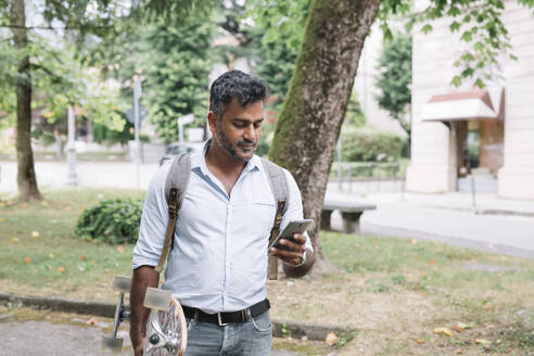 Lässiger Geschäftsmann mit Skateboard und Smartphone in der Stadt - ALBF01154