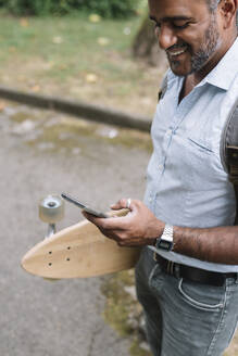 Glücklicher Geschäftsmann mit Skateboard und Smartphone in der Stadt - ALBF01155