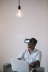 Businessman sitting at table testing VR simulator - ALBF01194