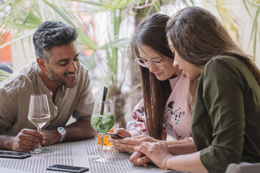 Friends sitting at table with drinks looking at smartphone - ALBF01201