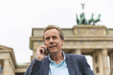 Portrait of smiling senior man on the phone at Brandenburg Gate, Berlin, Germany - WPEF02047