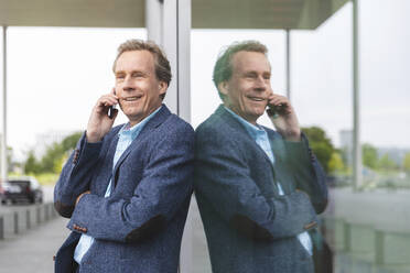 Porträt eines lächelnden älteren Geschäftsmannes am Telefon an einer Glasfront - WPEF02051