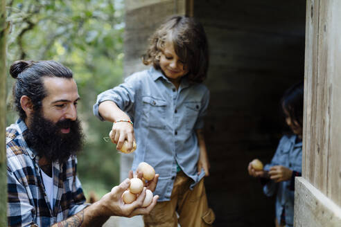 Father with two kids collecting eggs at chicken coop on an organic farm - SODF00095