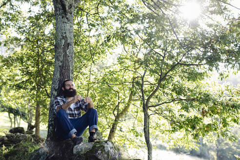 Mann mit Bart entspannt sich an einem Baumstamm im Wald - SODF00104