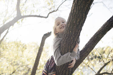 Portrait of smiling little girl climbing on tree in autumn - EYAF00589