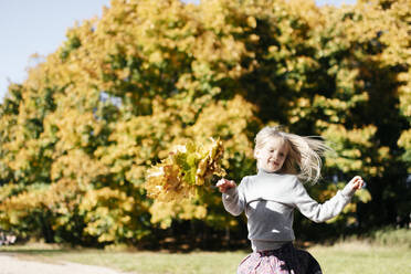Porträt eines lächelnden kleinen Mädchens, das mit einem Herbstkranz im Park läuft - EYAF00592