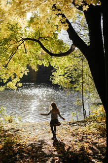 Rückenansicht eines kleinen Mädchens, das den Herbst am Flussufer genießt - EYAF00595