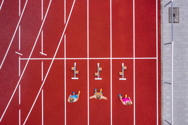 Germany, Baden Wurttemberg, Winterbach, Aerial view of three female sprinters standing at track starting block - STSF02298