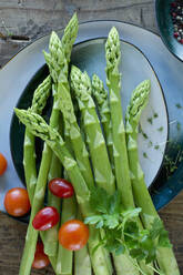 Plates and bowls with fresh cherry tomatoes, asparagus, parsley, cress and pepper - ASF06509