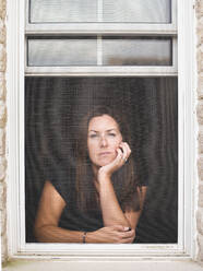 Woman looking out of open window with chin resting on hand. - CAVF65172