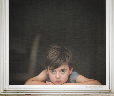 Junge, der durch den Schirm eines offenen Fensters hinausschaut., lizenzfreies Stockfoto