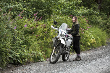 Eine Frau macht eine Pause vom Motorradfahren und steht bei ihrem Motorrad. - CAVF65202