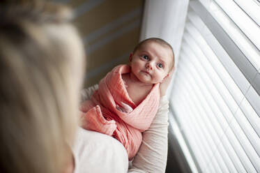 Blick von oben auf die Mutter, die ihre neugeborene Tochter hält und zum Fenster hinaufschaut - CAVF65221