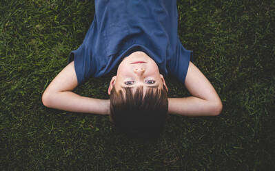 Upside down image of boy laying on grass with arms behind head. - CAVF65242