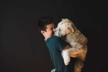 Ein Jugendlicher hält einen flauschigen Hund, der ihm das Gesicht leckt. - CAVF65246
