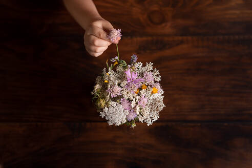 Mädchenhand platziert Wildblume in Vase von oben dunkler Hintergrund - CAVF65284