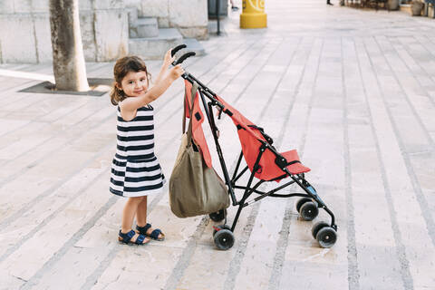 Porträt eines lächelnden kleinen Mädchens, das seinen Kinderwagen schiebt, lizenzfreies Stockfoto