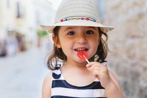 Porträt eines lächelnden kleinen Mädchens mit herzförmigem Lutscher im Sommer - GEMF03213