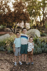 Portrait of three brothers smiling at camera in cactus garden - CAVF65303