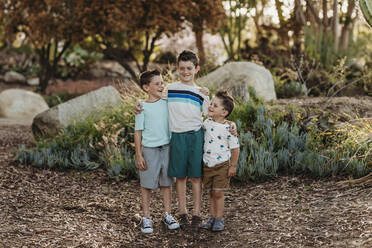 Portrait of three brothers smiling at each other in cactus garden - CAVF65304