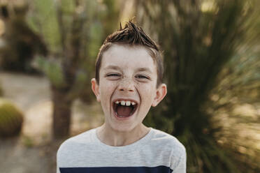 Close up portrait of cute young boy with freckles laughing outdoors - CAVF65313
