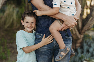 Mittelansicht eines Jungen im Grundschulalter, der Vater und Bruder umarmt und lächelt - CAVF65319