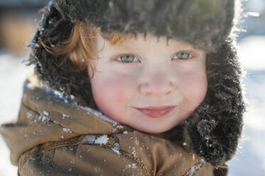 Porträt eines fröhlich lächelnden Kleinkindes mit Wintermütze und Jacke bekleidet - CAVF65333