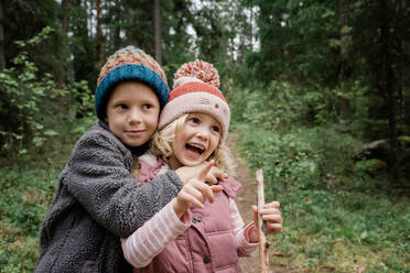 Brother hugging his sister laughing whilst walking through the forest - CAVF65334