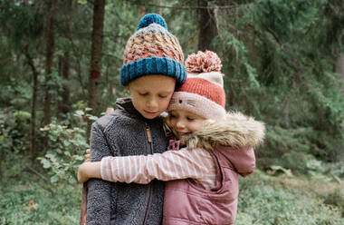 Bruder und Schwester umarmen sich beim Spielen im Wald - CAVF65335