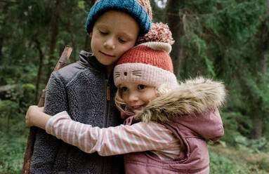 Bruder und Schwester, die sich umarmen, während sie gemeinsam im Herbst draußen spazieren gehen - CAVF65336