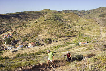 Spanien, Kanarische Inseln, La Gomera, Zwei Wanderer beim Aufstieg zum Tafelberg mit Dorf im Hintergrund - MAMF00869