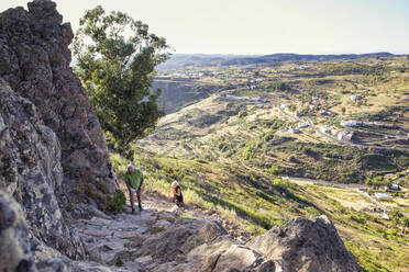 Spanien, Kanarische Inseln, La Gomera, Zwei Wanderer beim Aufstieg zum Tafelberg mit Bergdorf im Hintergrund - MAMF00870