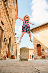 Freudiges Kind springt auf dem Bürgersteig in einer toskanischen Stadt auf - CAVF65344
