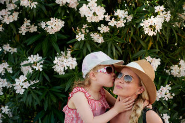 Daughter kissing mother near blooming bush - CAVF65359