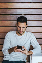 Porträt eines jungen Mannes, der in einem Café sitzt und ein Mobiltelefon benutzt - CAVF65375