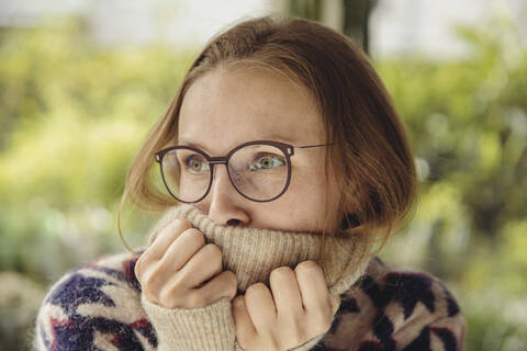 Junge Frau mit Brille und flauschigem Pullover schaut zur Seite, lizenzfreies Stockfoto
