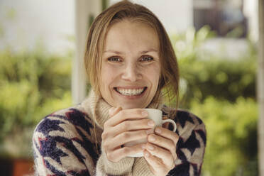 Portrait of smiling young woman wearing fluffy sweater holding a cup - MFF04883