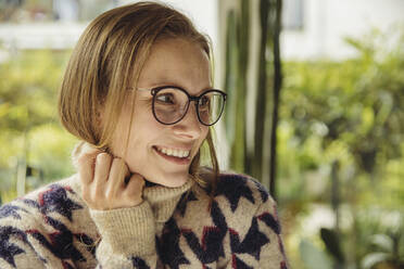 Porträt einer lächelnden jungen Frau mit Brille und flauschigem Pullover, die zur Seite schaut - MFF04885