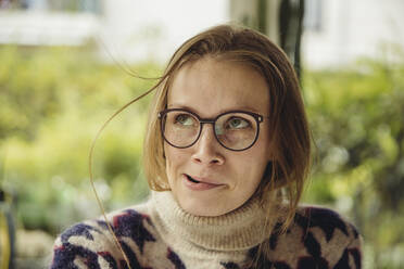 Porträt einer jungen Frau mit Brille und flauschigem Pullover, die eine Haarsträhne aufbläst - MFF04886