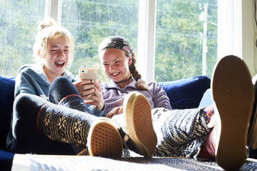 Teen girls laughing on a couch looking at something on a phone - CAVF65379