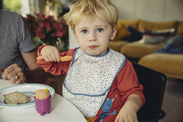 Porträt eines blonden kleinen Jungen, der ein Frühstücksei isst - MFF04888