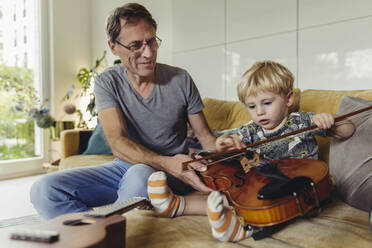 Porträt eines Kleinkindes, das eine Geige testet, während sein Vater zusieht - MFF04890