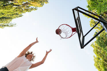 Niedriger Blickwinkel von Teenager-Junge spielt Basketball gegen klaren blauen Himmel - CAVF65416