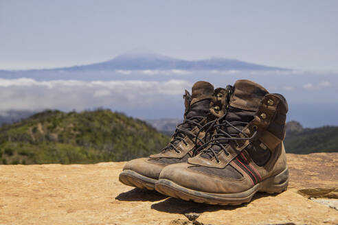 Spanien, Kanarische Inseln, La Gomera, Ein Paar braune Wanderschuhe stehen auf dem Gipfel des Garajonay mit dem Vulkan Teide in der Ferne - MAMF00892