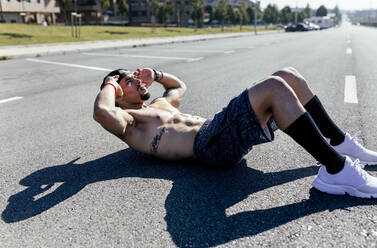 Junger Mann macht Sit-ups auf einer Straße - MGOF04142