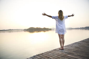 Rear view of mature woman standing on jetty at a lake at sunrise - PNEF02174