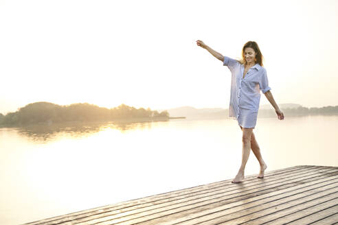 Mature woman balancing on jetty at a lake at sunrise - PNEF02184